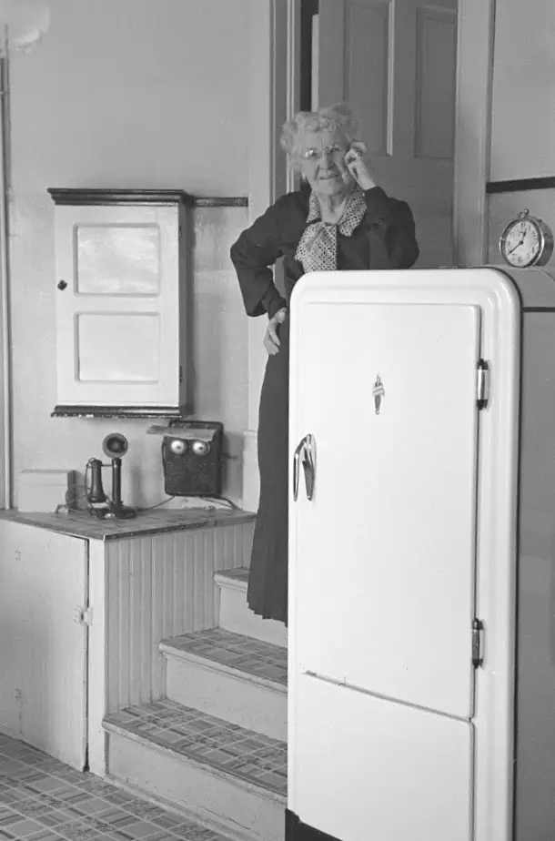 black and white photo of woman next to old refrigerator