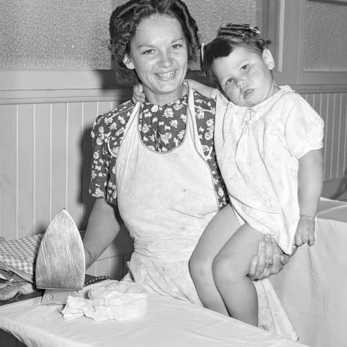 1940s housewife ironing and holding child