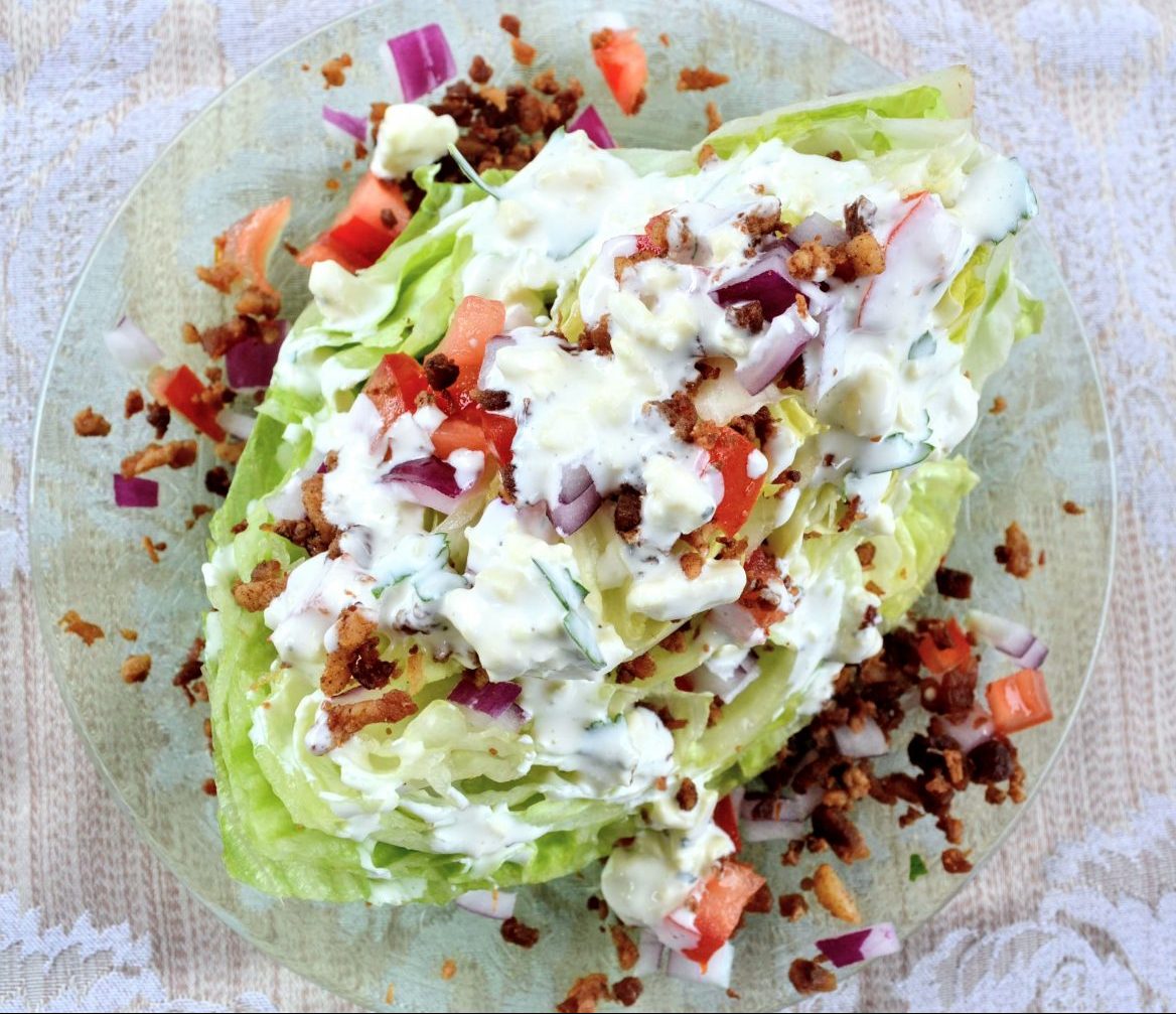 wedge salad on glass plate with dressing, bacon, tomato, and onion