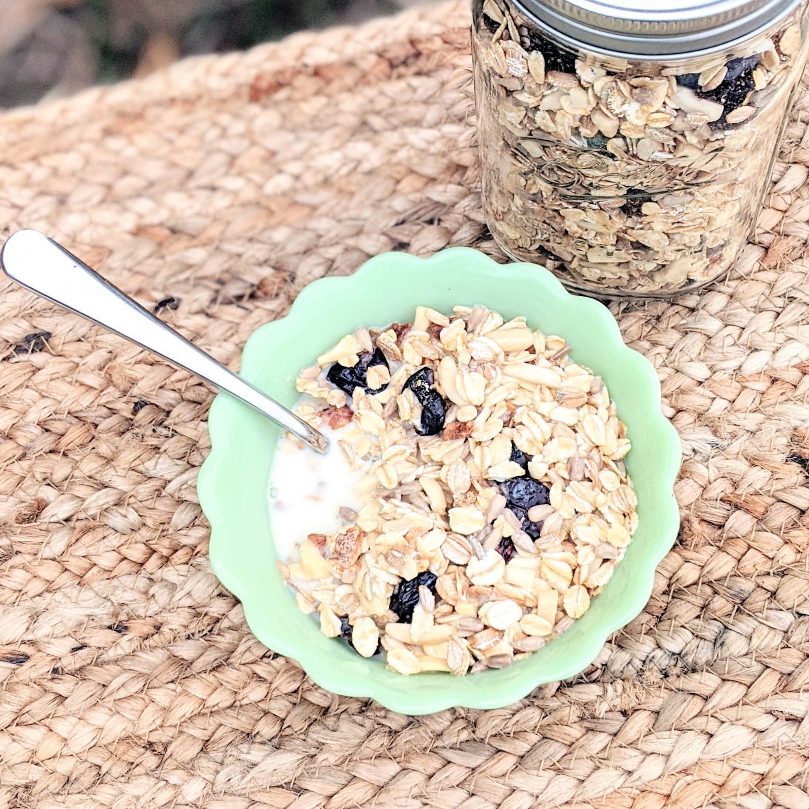 muesli in green bowl with milk and mason jar full of muesli on table