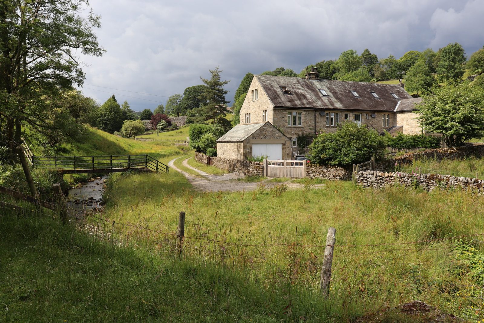 old stone farm buildings nestled in valley of green grass